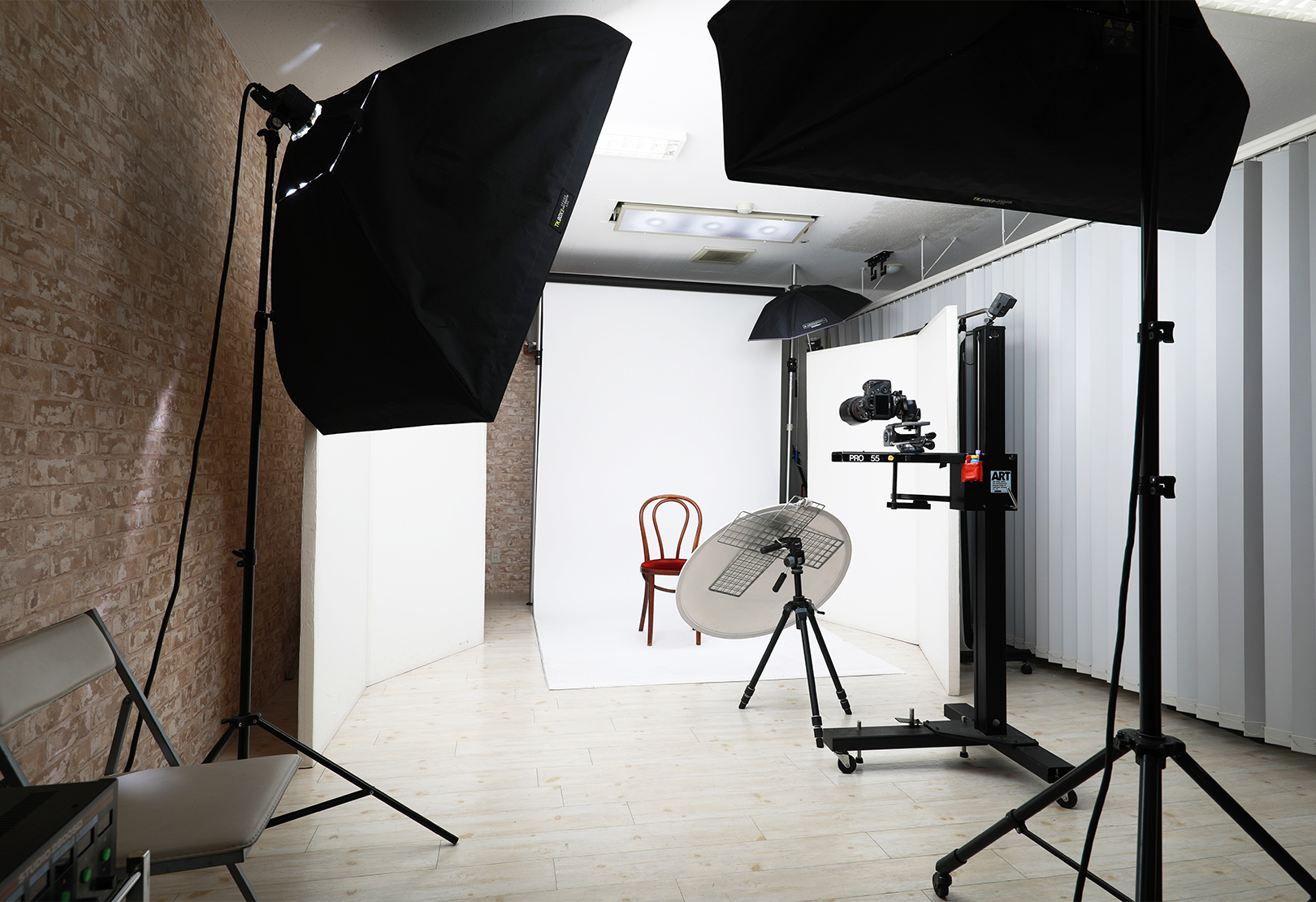 スタジオの内部を映しており、大型ソフトボックス、無限壁の背景、中央の赤い椅子、カメラとリフレクターが配置された清潔で明るい空間